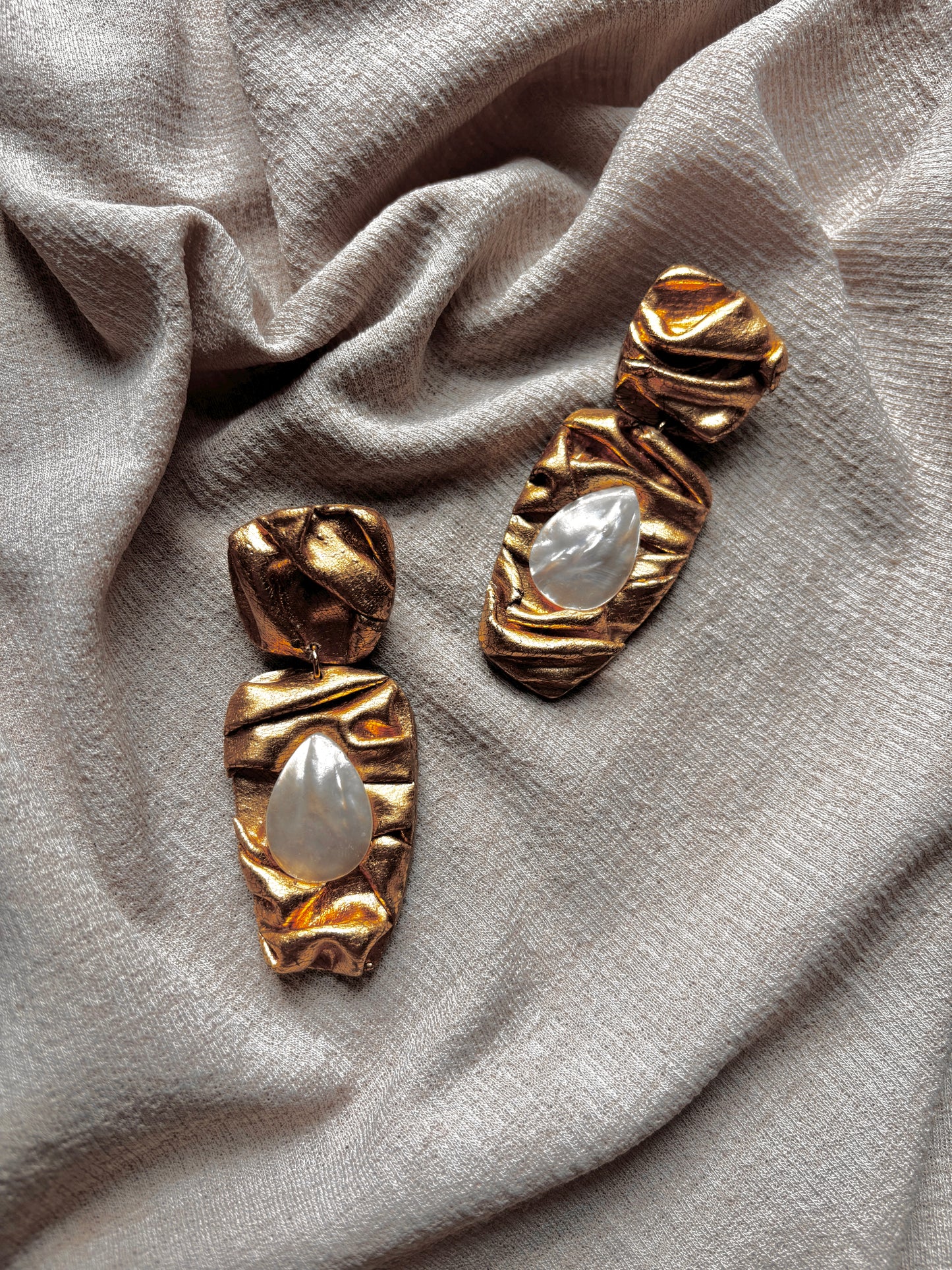 Gold earrings with pearl-like centers on a beige fabric background