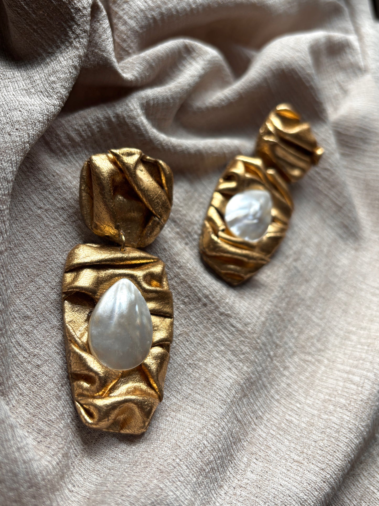Gold earrings with white stones on a light fabric background
