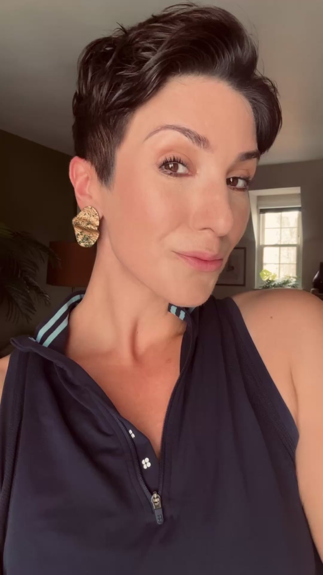Model wearing Ava & Azar handcrafted vida wave stud statement earrings emerald green and gold